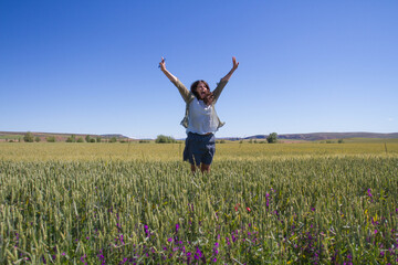 Fototapeta na wymiar Happy middle-aged woman jumping in the wheat fields. Optimism and enthusiasm