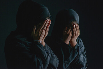 Muslim woman in black hijab, both hands touched her face as she prayed on black background