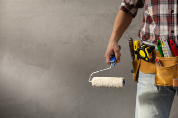 Construction worker man holding paint roller tool near concrete or plaster wall. Male hand and tools