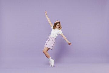 Fototapeta na wymiar Full length little hppy blonde kid girl 12-13 year old in white shirt stand on toes with outstretched hands leaning back dance isolated on purple color background Childhood children lifestyle concept