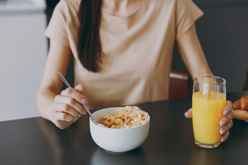 Cropped up portrait shot photo of young housewife woman 20s wearing casual clothes beige shirt eat oatmeal porridge muesli cooking food in light kitchen at home alone. Healthy diet lifestyle concept