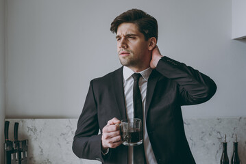 Young puzzled thoughtful employee business man corporate lawyer 20s in formal black suit shirt tie drink coffee breakfast look aside scratch neck in light kitchen Achievement career lifestyle concept