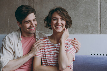 Young happy smiling couple two friends woman man 20s in casual clothes sitting on sofa talking with each other boyfriend hug girlfriend resting indoors at home flat together. People lifestyle concept