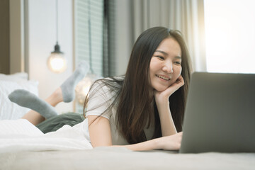 Obraz na płótnie Canvas happy Young asian woman working with laptop in bed at home in the morning. lifestyle concept