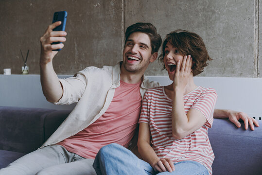 Young couple two friends woman man 20s in casual clothes sitting on sofa do selfie shot mobile phone post photo social network hold face rest indoors at home flat together People lifestyle concept