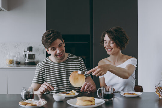Young happy couple two woman man in casual t-shirt clothes sit by table eat pancakes maple syrup have breakfast in morning cook food in light kitchen at home together Healthy diet lifestyle concept.