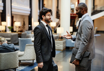 Side view portrait of two successful businessmen discussing work while standing in hotel lobby,...