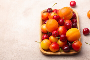 Naklejka na ściany i meble Wooden tray with fresh cherries, plums and apricots with water drops