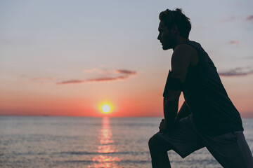 Silhouette side profile view young strong sporty athletic toned fit sportsman man in sports clothes warm up training at sunrise sun dawn over sea beach outdoor on pier seaside in summer day morning.