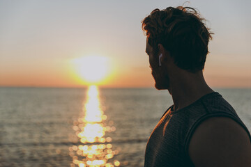 Close up side view young strong sporty athletic toned fit sportsman man in sports clothes earphones warm up training at sunrise sun dawn over sea beach outdoor on pier seaside in summer day morning