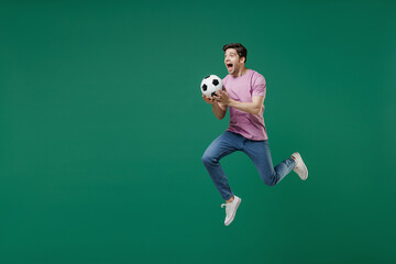 Fototapeta na wymiar Full size body length young fun man fan wear pink t-shirt cheer up support football sport team hold in hand soccer ball watch tv live stream scream jump isolated on dark green color background studio.
