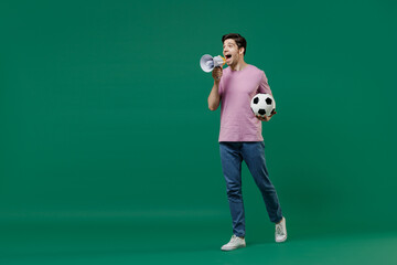 Naklejka na ściany i meble Full size length young crazy fun man fan wears basic pink t-shirt cheer up football sport team hold soccer ball watch tv live stream scream in megaphone isolated on dark green color background studio.