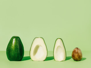 Whole fresh avocado fruit and two halves  in a row with a seed isolated on a mint green background....