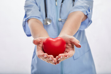 Close up of female doctor hands holding the heart. Red heart showing by woman doctor wearing blue medical face mask and lab coat with a stethoscope. Cardiology, healthcare, and medicine concept.