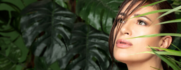 Beauty and skin care concept with a beautiful woman face amongst green tropical leaves. Wellness, natural beauty and skin care or spa treatments