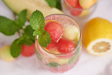 Refreshing summer citrus cocktail with lemon, watermelon and melon with mint and ice cubes in...