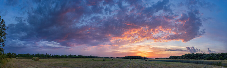 A rolls of hay in field at sunrise with amazingly beautiful clouds.