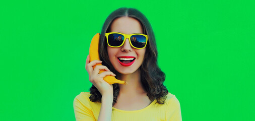 Portrait close up of funny young woman calling on a banana phone on green background
