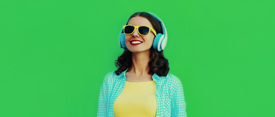 Portrait close up of happy smiling young woman listening to music in wireless headphones on a green background