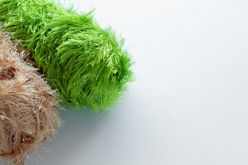 Nylon or acrylic elongated large balls with a long thick pile of green and beige colors for knitting handmade and hobbies on a white fabric background on the left in the frame and copy space
