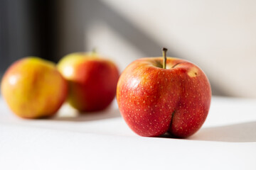 Bright ripe apple of an unusual shape buttocks in the light of the sun on a white background with ordinary apples behind. Nonconformism, body positive, dissimilarity, uniqueness concepts