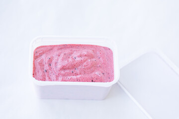 Berry ice cream pink color cream texture in a rectangular white container with an open lid on a white background. Top view