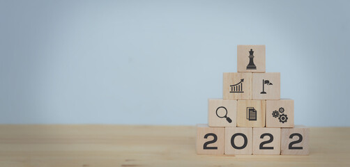 Business strategy and planning concept in 2022 for business development.  Wood cubes block with strategy, goal, performance, solution, teamwork icon on the table with grey background and copy space.
