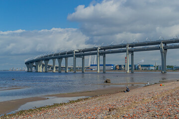 View of the rounded motorway highway bridge against a background of blue sky with clouds. The road passing over the sea bay near the coast of the city. Saint Petersburg, Europe