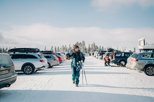 Kvinna g&aring;r med skidor p&aring; bilparkering och tittar bort