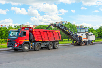 Road cold milling machine removes the old asphalt and loading into a dump truck. Repair of asphalt pavement of the road. - obrazy, fototapety, plakaty