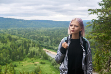 teenage girl with a backpack walks along the top of the mountain against the backdrop of wooded hills