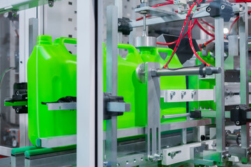 Empty green plastic jerrycans moving on conveyor belt of automatic pet blow molding machine at factory, exhibition. Manufacturing, recycling, industry, automated technology equipment concept - obrazy, fototapety, plakaty