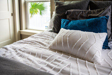 Closeup of new bed comforter with decorative white blue pillows in bedroom in staging home, house or apartment modern style