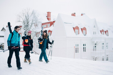 Leende vänner går med skidorna på axlarna i stad