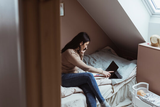 Kvinna pratar i mobiltelefon och l&auml;ser p&aring; datorsk&auml;rm i sovrum