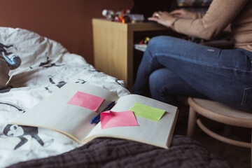 Öppen anteckningsbok ligger på säng bredvid arbetande kvinna
