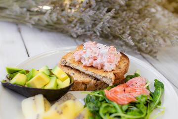 Toast salmon mayonnaise and spice  with salad, avocado and kiwi on wooden table. Healthy breakfast concept. 