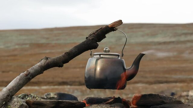 Camp kettle boiling on bonefire in the mountains. Lapland. Camping or adventure trip scenery concept. 