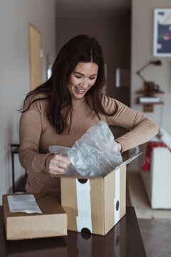 Glad kvinna &ouml;ppnar paket p&aring; b&auml;nk i k&ouml;k