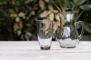 Glass jug and tall glass on wooden table with garden tree on background with copy space.