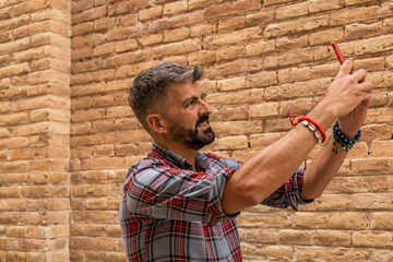 Portrait of a bearded man taking selfie outdoor against brick wall