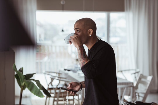 Man st&aring;r med smartphone i handen och dricker kaffe