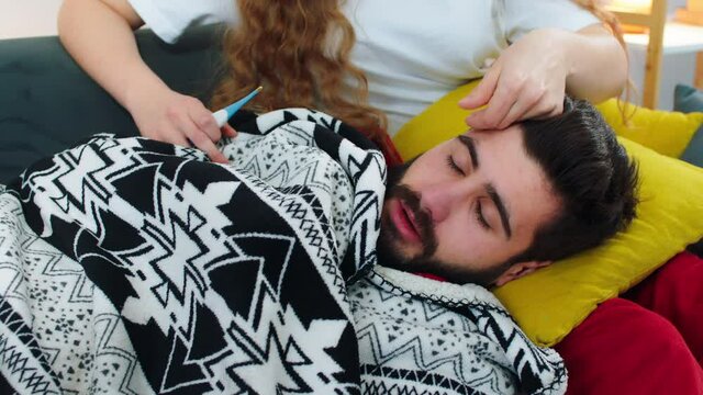 A young man laying his head on a pillow on a woman s lap, his face is red from feeling cold and having the flu