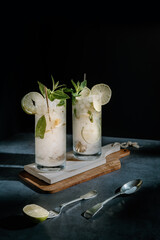 Dark photography of a cold drink, a glass of mojito with mint leaf, ice, lemon and sugar on a wooden table with a vintage style.