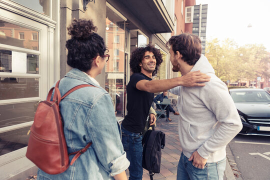 Leende v&auml;nner h&auml;lsar p&aring; trottoar i stad