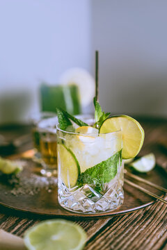 Bright photography of a cold drink, a glass of mojito with mint leaf, ice, lemon and sugar with tequila shots on a wooden table with copyspace