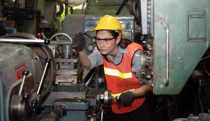 Portrait of confident young female mechanical worker in a protective uniform, helmet controls the CNC Machinery while working at the plant.