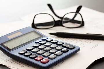 calculator, glasses, pen and papers on white fading background with copy space. Business concept.