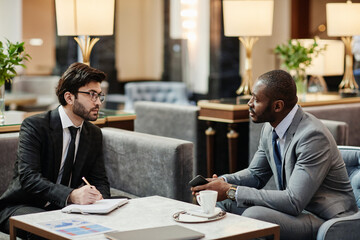 Side view portrait of two business partners discussing deal in luxurious hotel lobby, copy space
