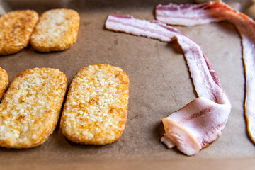 Macro closeup of baking sheet with parchment paper for hash browns shredded potatoes and raw uncooked bacon strips